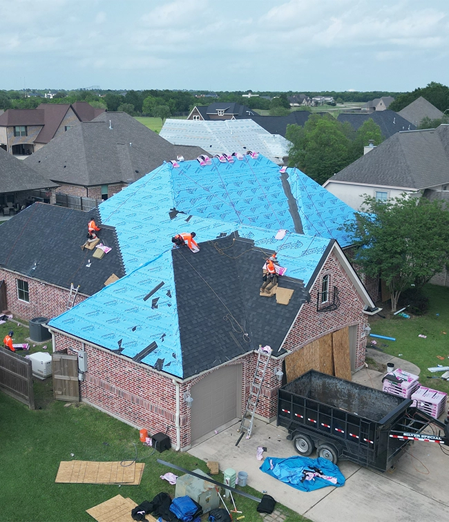 Aerial view of TX Roofing crew members laying new underlayment and shingles on a brick home