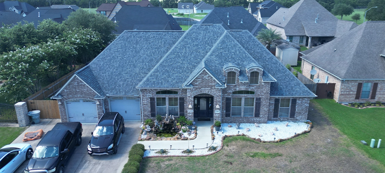 Aerial view of a brick home with a two-car garage and a new slate gray shingle roof