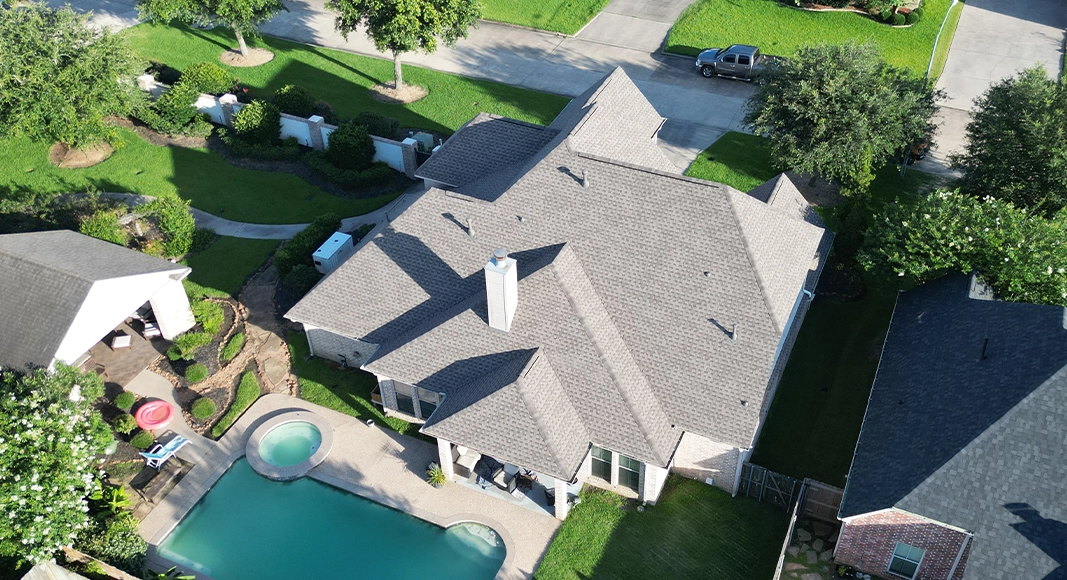Aerial view of a home with a backyard pool and a new light gray shingle roof