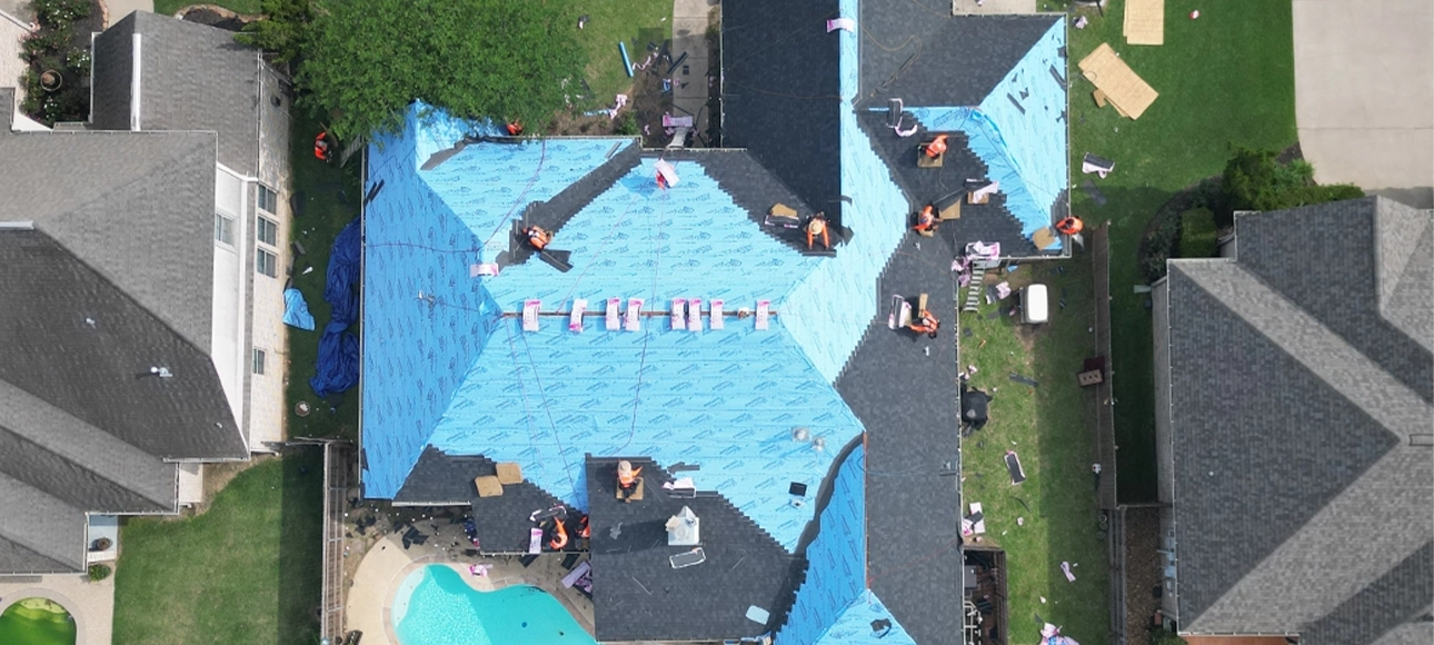Crew members working across the same roof covered in blue synthetic underlayment