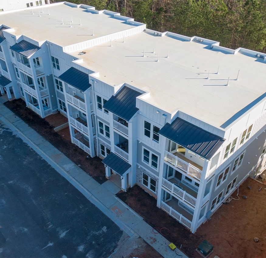 Aerial view of a three-story apartment building with a white flat commercial roof
